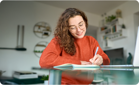 Estudiante tomando apuntes en casa con un jersey naranja